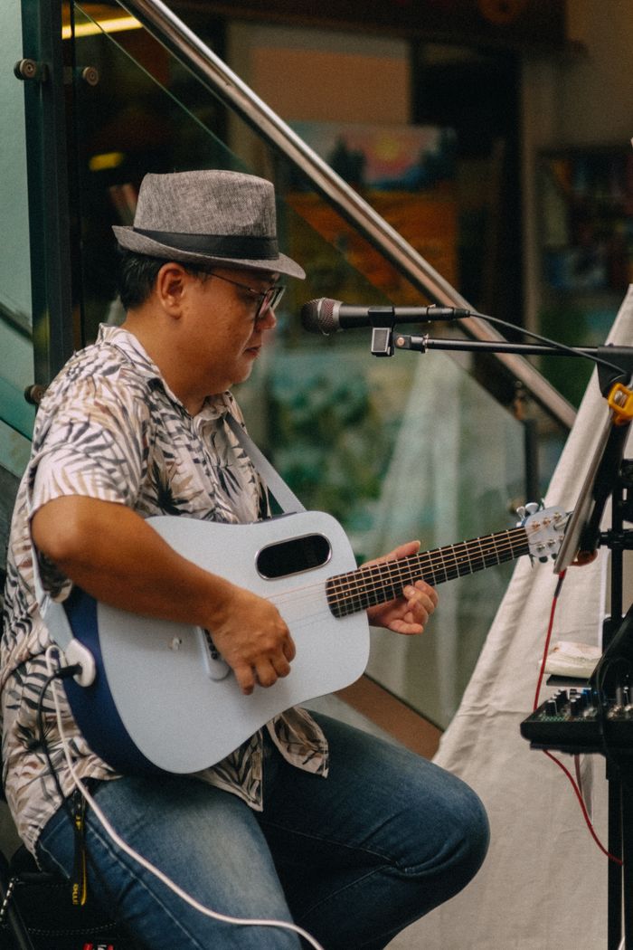 menu-02 A musician strumming an acoustic guitar during an outdoor performance.