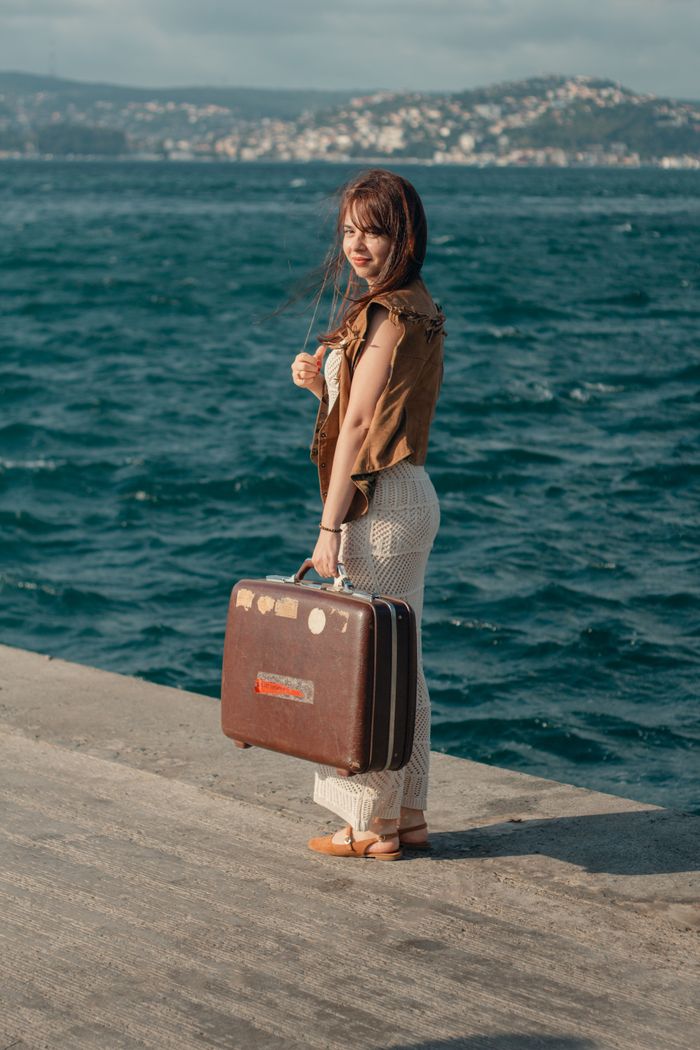 menu-17 A woman holds a vintage suitcase by the sea in Istanbul, capturing a moment of travel and exploration.