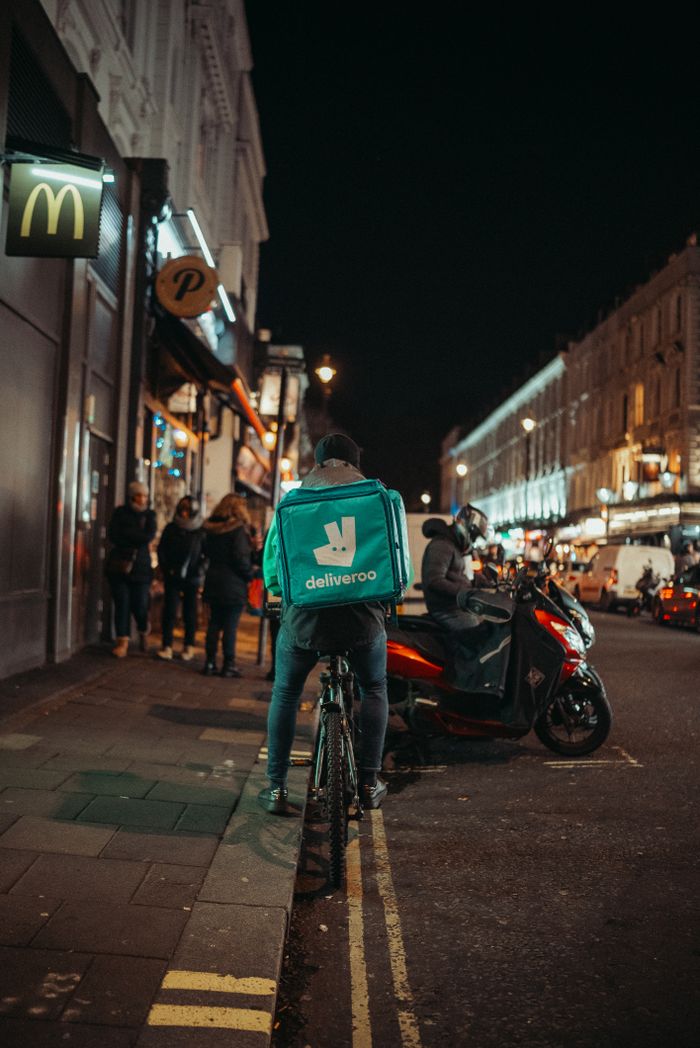 about-02 Urban street at night featuring a delivery cyclist parked by the sidewalk.