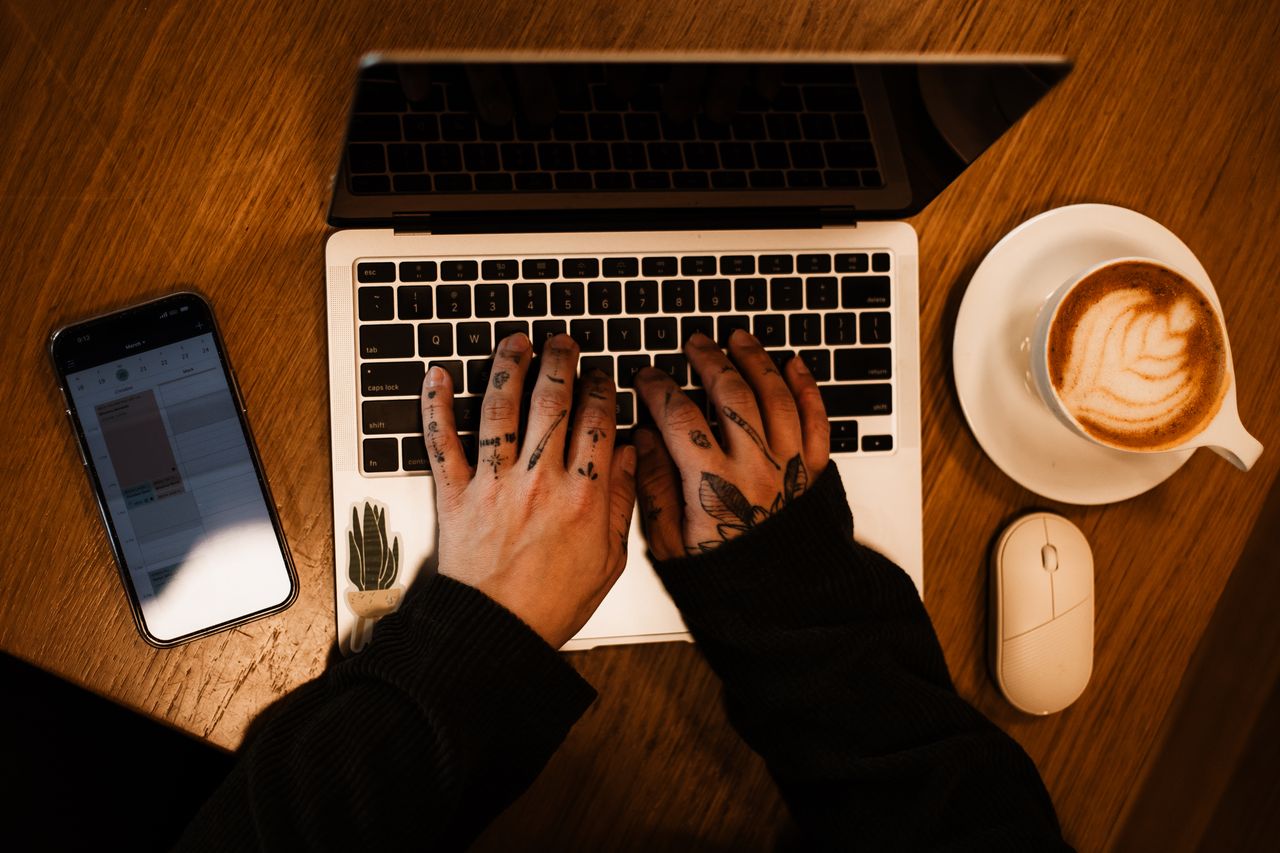 about-03 Tattooed hands on a laptop with coffee and phone, perfect workspace inspiration.