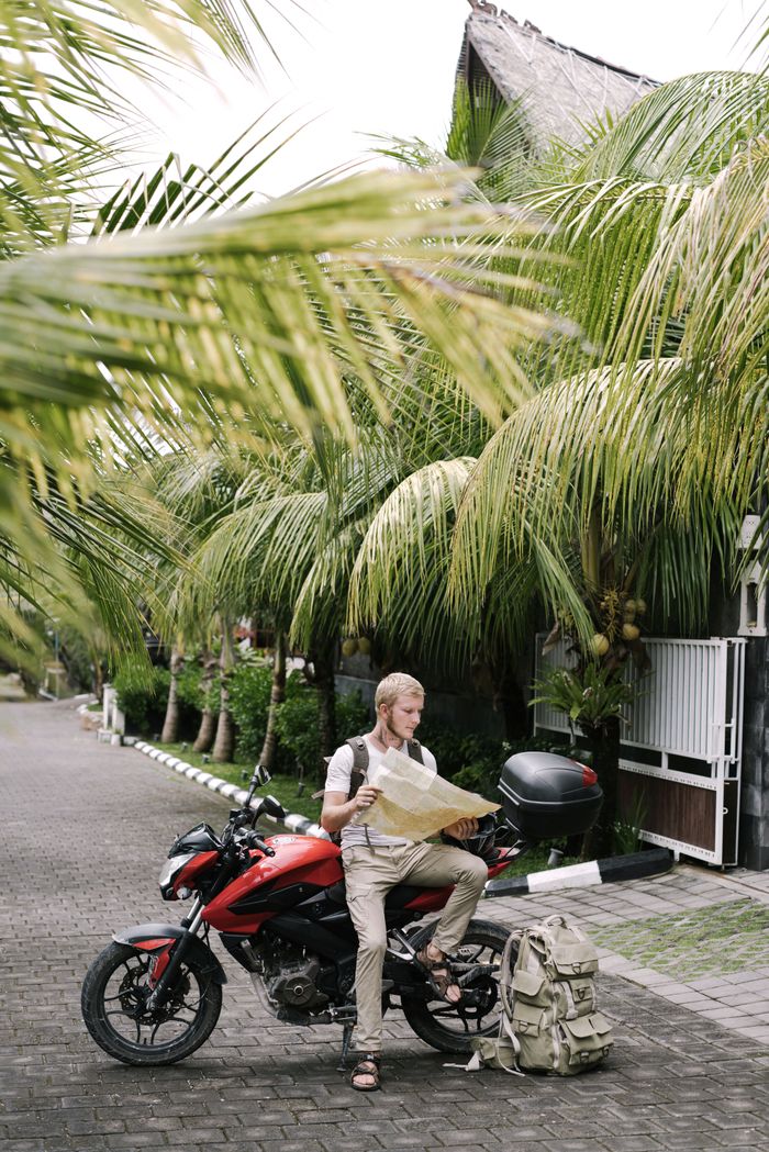 The Art of Drawing Readers In: Your attractive post title goes here Full length male traveler studying map of city while leaning on motorcycle near duffle bag on street pavement among palms branches