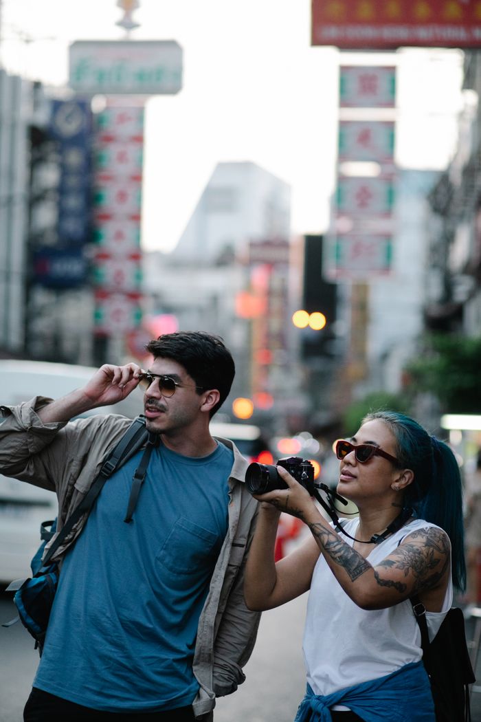 menu-14 Two stylish travelers explore the bustling city streets, capturing moments with a camera.